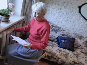 The senior woman holding gas bill in front of heating radiator. Payment for heating in winter.